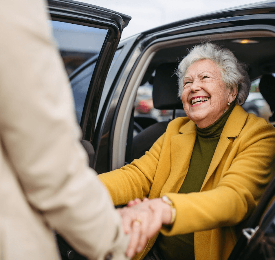 Senior woman smiling while getting out of a car with assistance